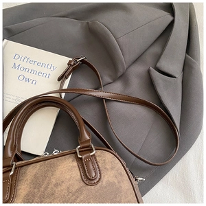 Close-up of vintage brown patchwork pillow bag on a suit, featuring leather straps and silver hardware