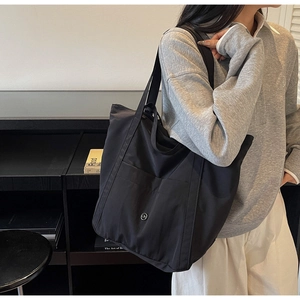Close-up of black nylon tote bag with round metal logo and large front pocket detail