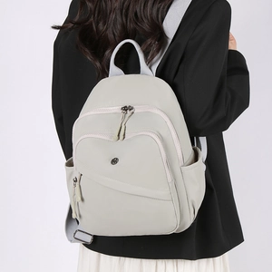 Rear view of model wearing a light grey waterproof nylon backpack with multiple compartments