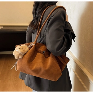 Detailed view of brown suede tote bag with decorative buckle and plush bear charm