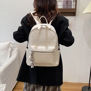 White woven faux leather backpack with metallic bear charm on woman's back in warm indoor setting