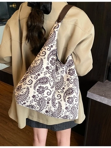 Large paisley canvas tote bag with brown shoulder strap worn by a model in casual style