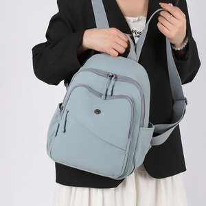 Close-up of light blue nylon backpack featuring multiple front zipper pockets and gray straps