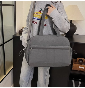 Detail of grey travel bag featuring adjustable shoulder strap and large front zip pocket