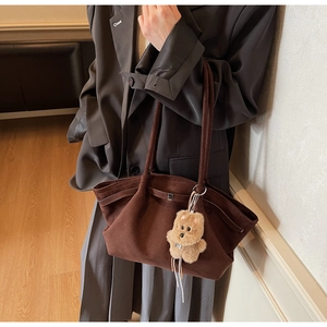 Detail of dark brown suede tote bag featuring a cute plush bear pendant on the strap