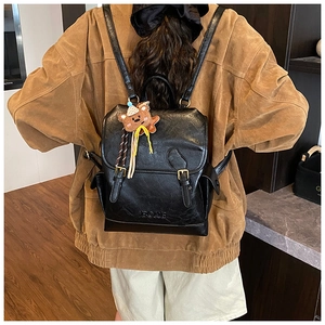 Detail view of black faux leather backpack on a model with a cute brown bear charm