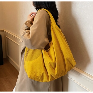 Détail d'un grand sac hobo en nylon jaune vif porté en bandoulière dans une pièce