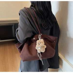 Detail of dark brown suede tote bag with plush bear charm worn over the shoulder