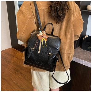 Detail of black vintage leather backpack with adjustable straps and cute bear charm