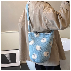 Blue faux shearling bucket bag with cute sheep pattern worn across the body by a model