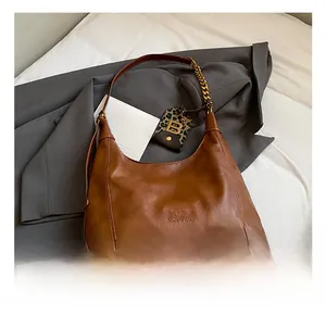 Detailansicht der braunen Ledertasche mit Logo-Prägung und goldener Kettenverzierung
