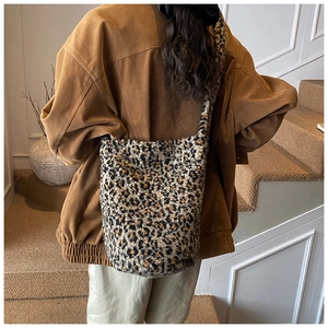 Model wearing a large leopard print plush bucket bag with soft faux fur texture and wide strap