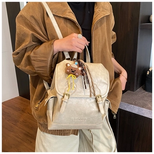 Detail of beige faux leather backpack with textured finish and cute plush bear charm