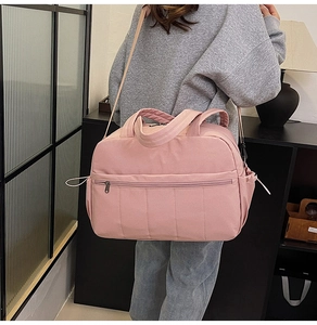 Detailed view of a pink travel bag featuring a reinforced handle and adjustable shoulder strap