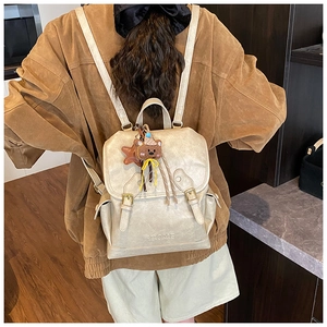 Rear view of a beige faux leather backpack with gold hardware and a cute bear charm