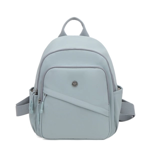 Detail of light blue nylon backpack with front zipper pocket and metal logo plaque