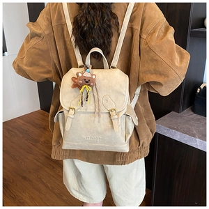 Rear view of model wearing a vintage beige backpack with a plush bear charm on wood floor