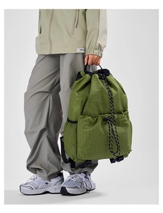 Detail of green checkered drawstring backpack showing side mesh pockets and front pouches