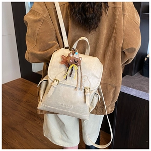 Detailed view of beige faux leather backpack with buckle closure and plush bear charm