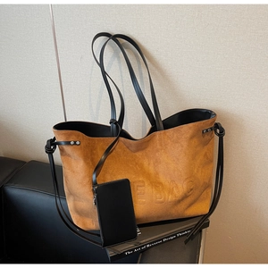 Dettaglio borsa tote in pelle scamosciata marrone con scritta THE BAG e manici neri