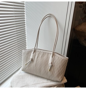 Détail d'un sac cabas plissé crème avec poignées à nœuds décoratifs et accents dorés