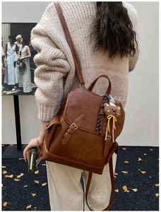 Detailed view of a brown vintage leather backpack featuring a cute bear charm and logo