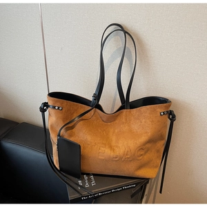 Dettaglio di borsa tote in pelle scamosciata marrone con manici neri e goffratura