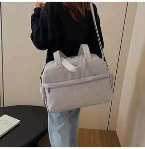 Detail view of a large grey travel bag with front zippers and side pockets shown on a model