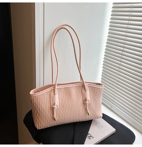Détail du sac à main rose clair à texture ondulée avec nœuds et fines bretelles