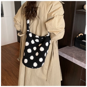 Detailed view of plush black and white polka dot bucket bag worn with a beige trench coat