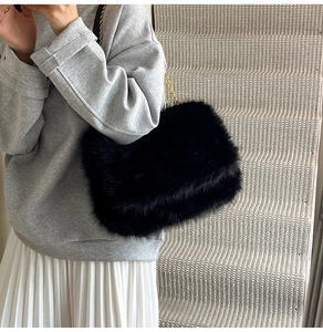 Detail of black faux fur shoulder bag with gold chain strap on grey sweater outfit