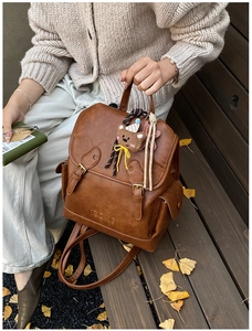 Detail of retro brown leather backpack with buckle straps and a cute teddy bear charm