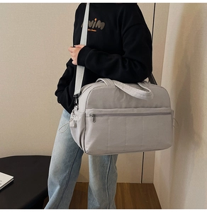 Model wearing a light grey quilted travel bag with large zipper pocket and side pockets