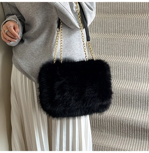 Close-up of black faux fur shoulder bag with golden chain straps on casual model
