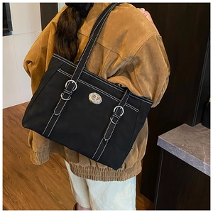 Detail of black canvas tote bag with contrast stitching and silver metal swivel lock