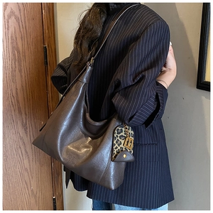 Detail der dunkelbraunen Leder-Hobo-Tasche mit Logo-Prägung und Leoparden-Anhänger