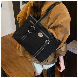 Detail of black tote bag featuring white contrast stitching and silver turn-lock closure