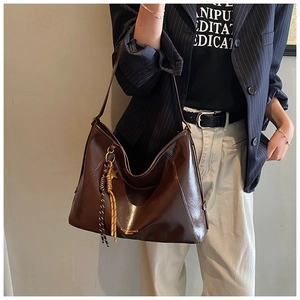 Détail d'un grand sac cabas marron avec breloque étoile et pompon, porté par un modèle
