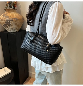 Détail d'un sac à main noir plissé avec boucles dorées et bandoulière à nœud cuir