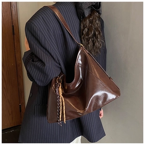 Détail du sac hobo marron brillant avec pompon tissé et lettrage sur le côté