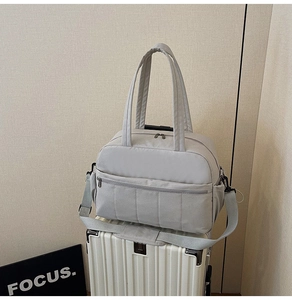 Detail of grey quilted travel bag placed on a suitcase showing fabric texture and zippers