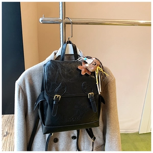 Detail of a vintage black leather backpack with gold buckles and a cute teddy bear charm