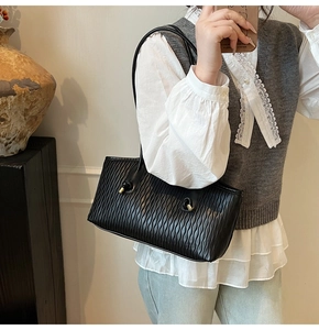 Détail du sac plissé noir avec des plis verticaux et des accents de boucles métalliques dorées