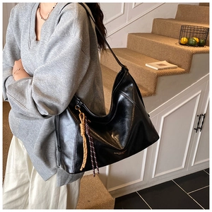 Détail d'un grand sac cabas noir brillant avec pendentif à pompon tissé porté par un mannequin