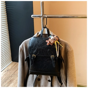 Detail of black vintage leather backpack with dual buckle straps and a cute teddy charm