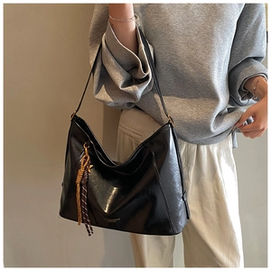 Détail du sac hobo en cuir noir avec ferrures dorées et breloque pompon tressée