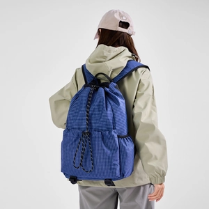 Blue plaid drawstring backpack shown from a back view on a model in a beige coat