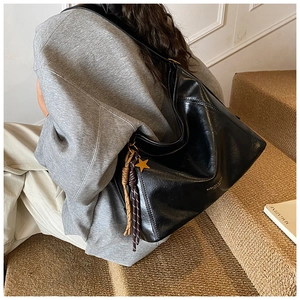 Détail du cabas en cuir noir brillant avec breloque étoile dorée et pompon tissé élégant