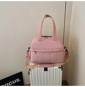 Detail of pink travel bag with dual handles and shoulder strap on top of a suitcase