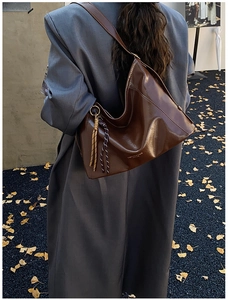 Détail d'un grand sac hobo en cuir souple marron foncé avec breloque en corde sur l'épaule